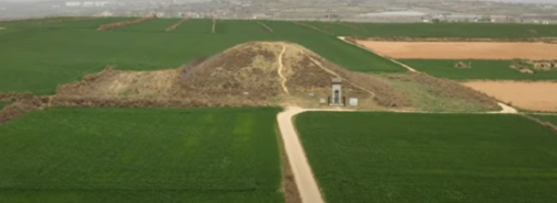 Large mound with a pathway leading to it and a stone structure in front.