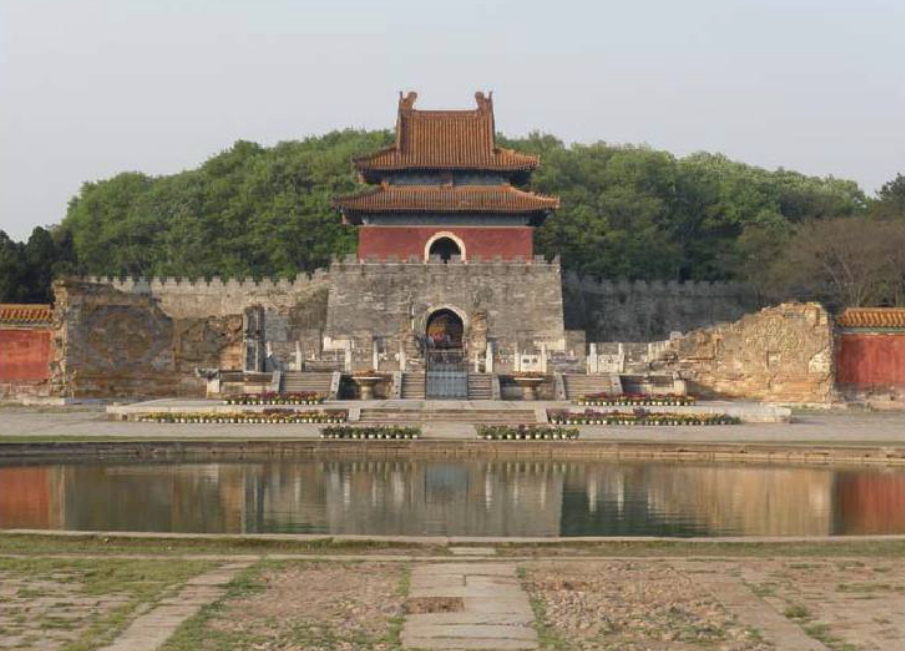 A red building surrounded by a stone wall and a water feature.